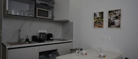 Una cocina moderna con microondas integrado, cafetera y un lavabo. Hay una mesa de comedor con sillas y un mueble pequeño debajo de la encimera.