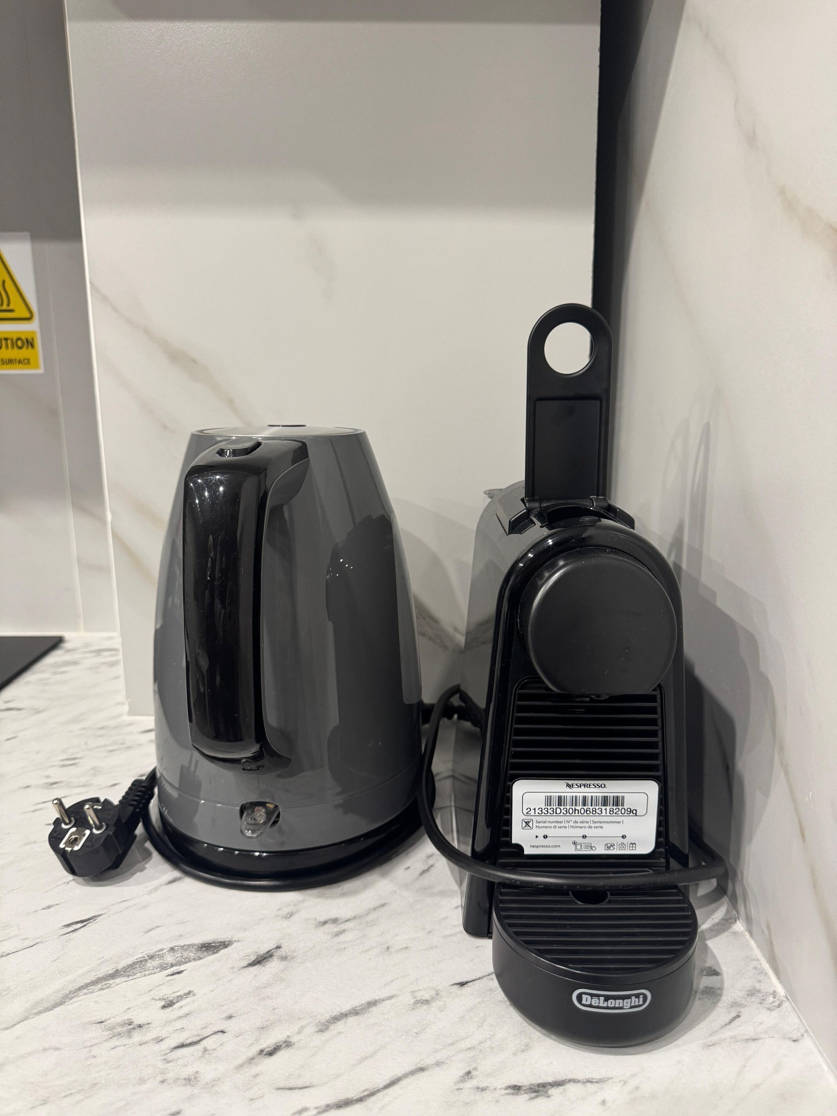A black electric kettle and a black coffee maker with a label on the coffee maker, placed on a marble countertop.