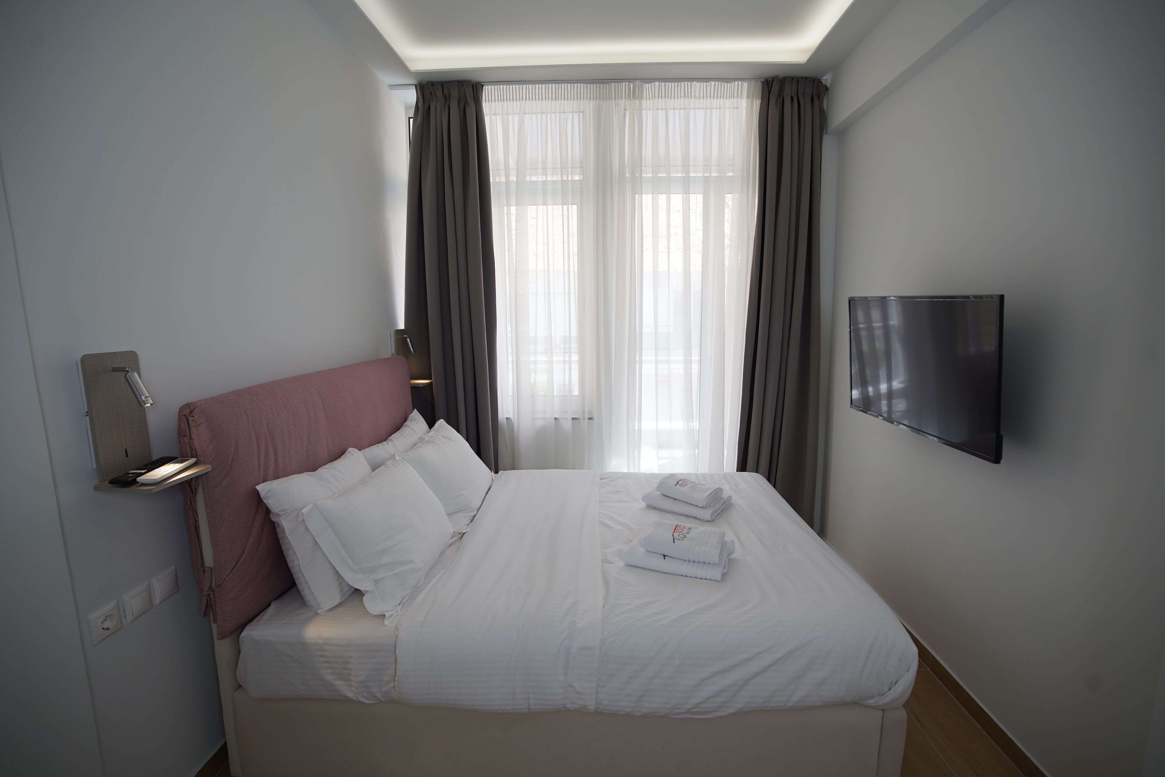 Een hotelkamer met een bed, een aan de muur bevestigde televisie en een raam met gordijnen.