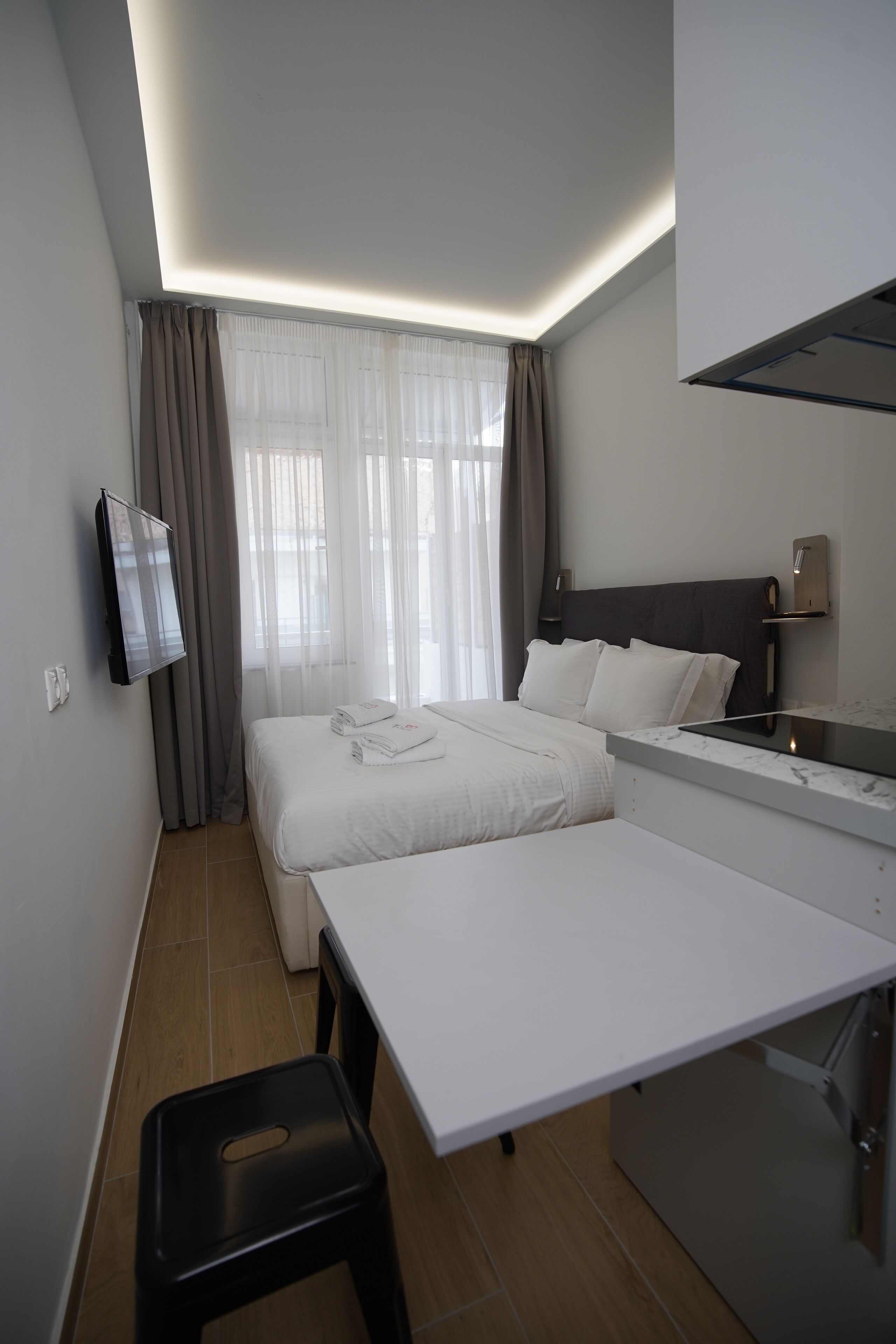A compact hotel room with a bed, a desk, a chair, a TV, and a window with curtains.