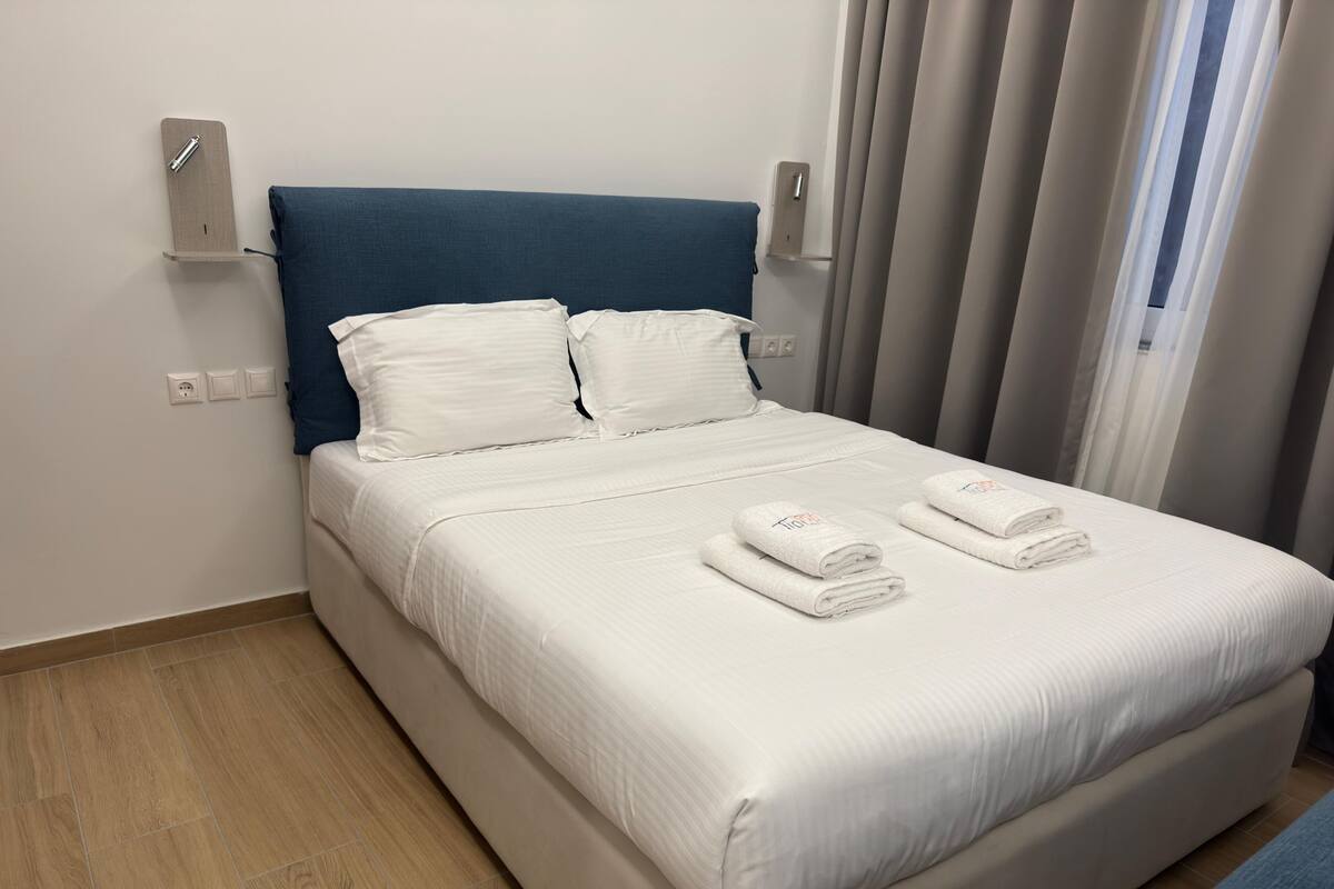 A neatly made bed with white linens and two folded towels, a blue headboard, and a wooden floor.