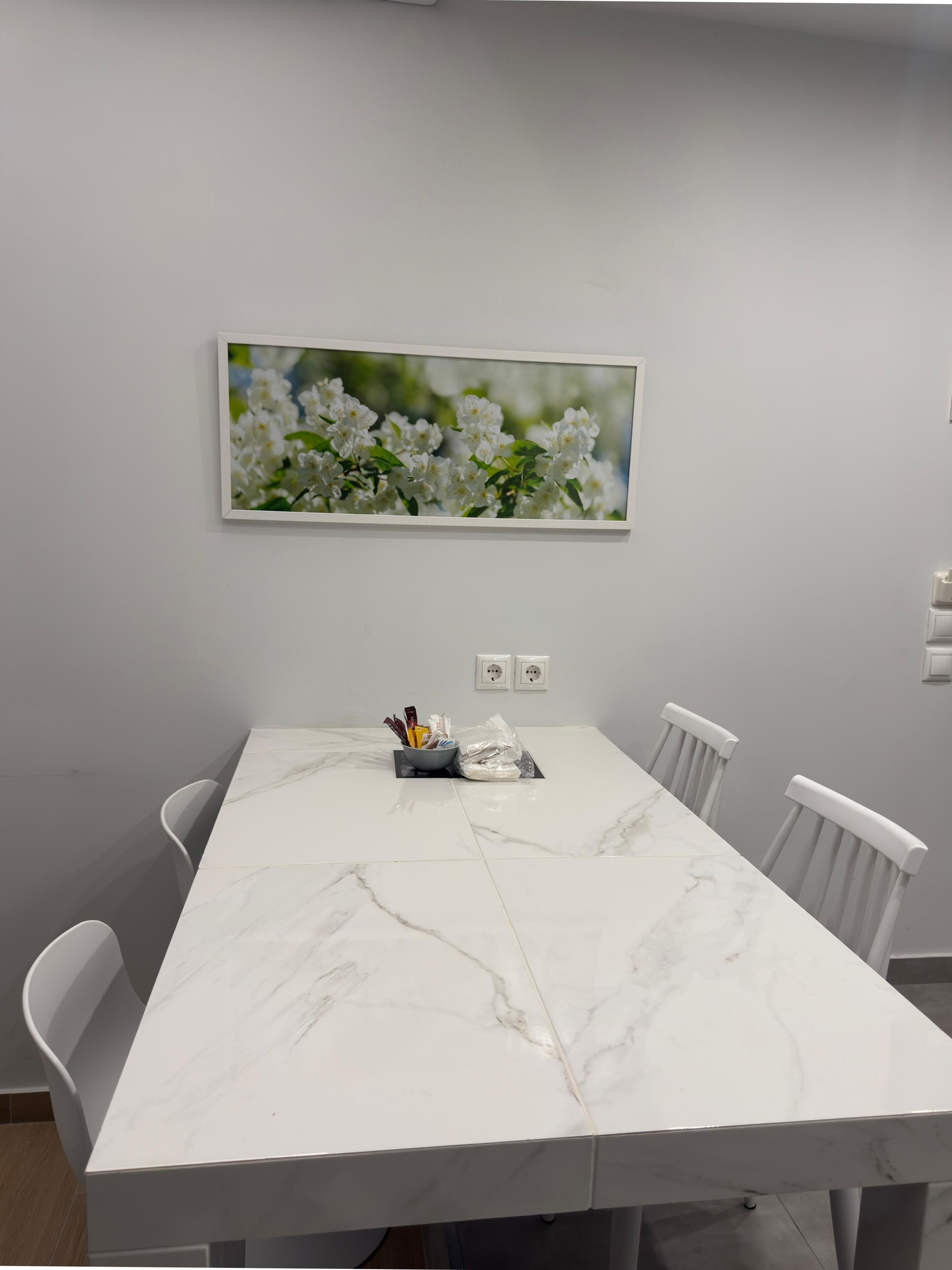 A conference room with a marble table, white chairs, a framed floral artwork on the wall, and a small bowl with utensils on the table.