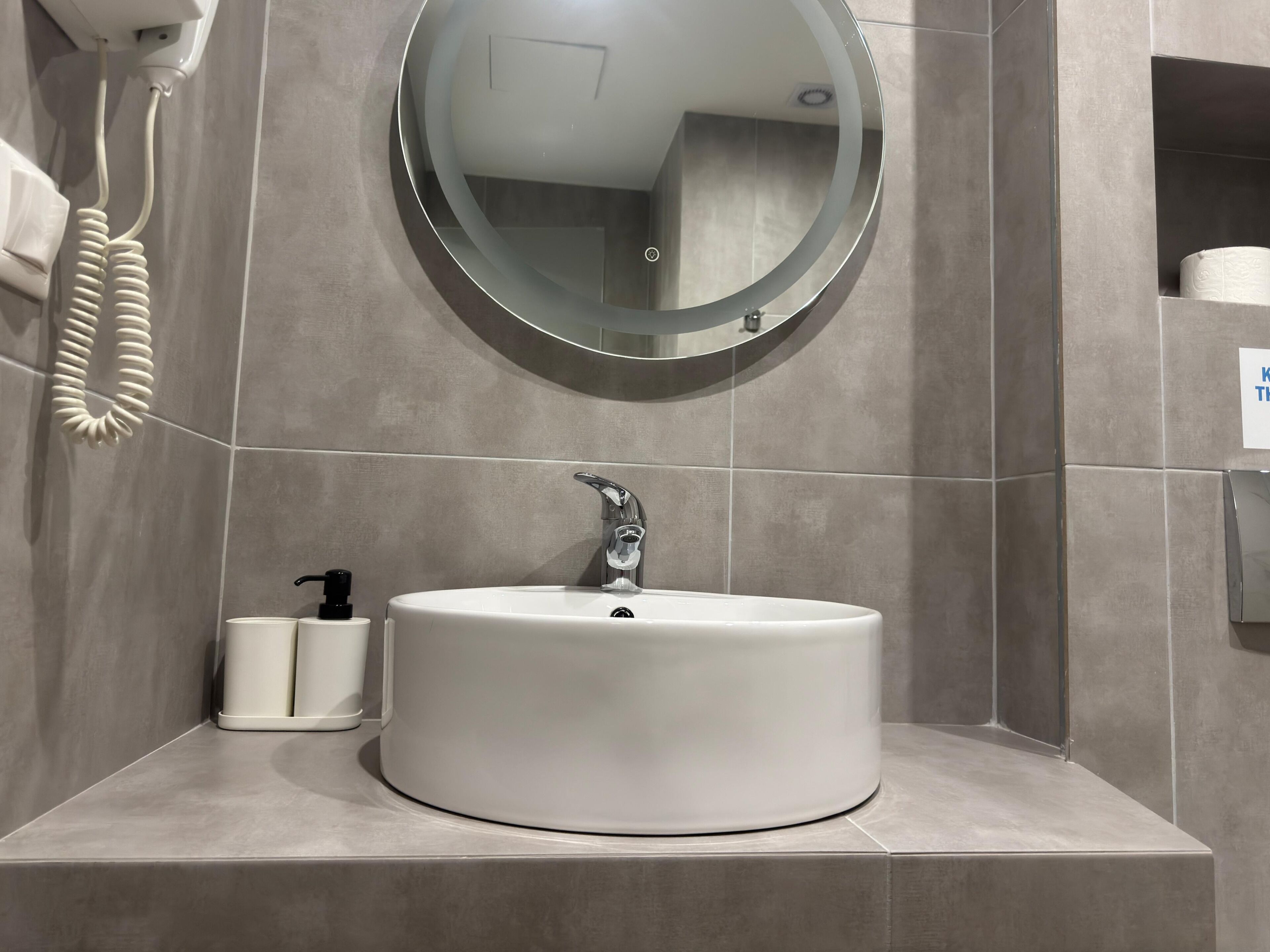 A bathroom with a round mirror, a white sink, and a toilet paper holder.
