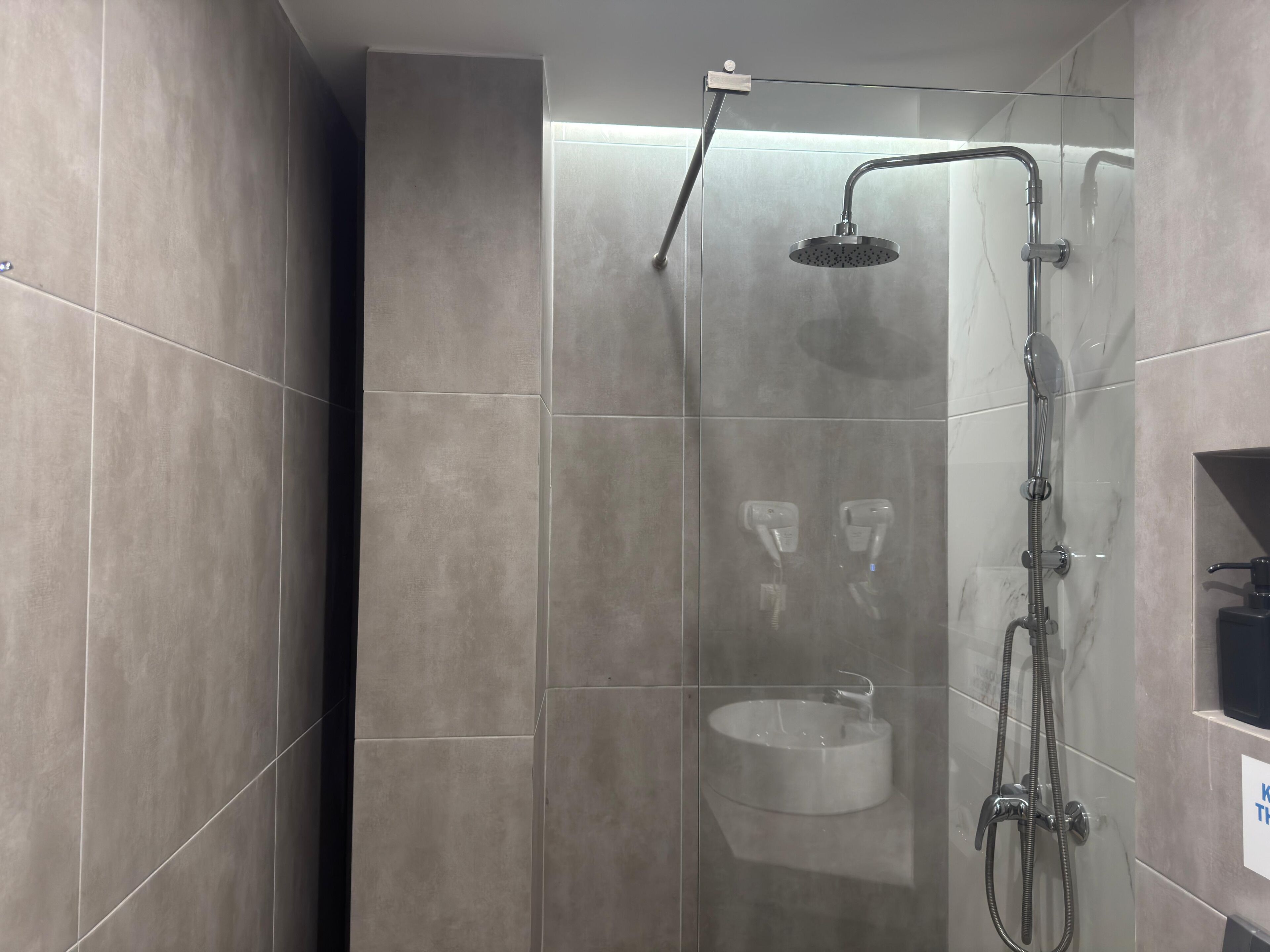 A modern shower area with a handheld showerhead, a fixed showerhead, and a wall-mounted sink.