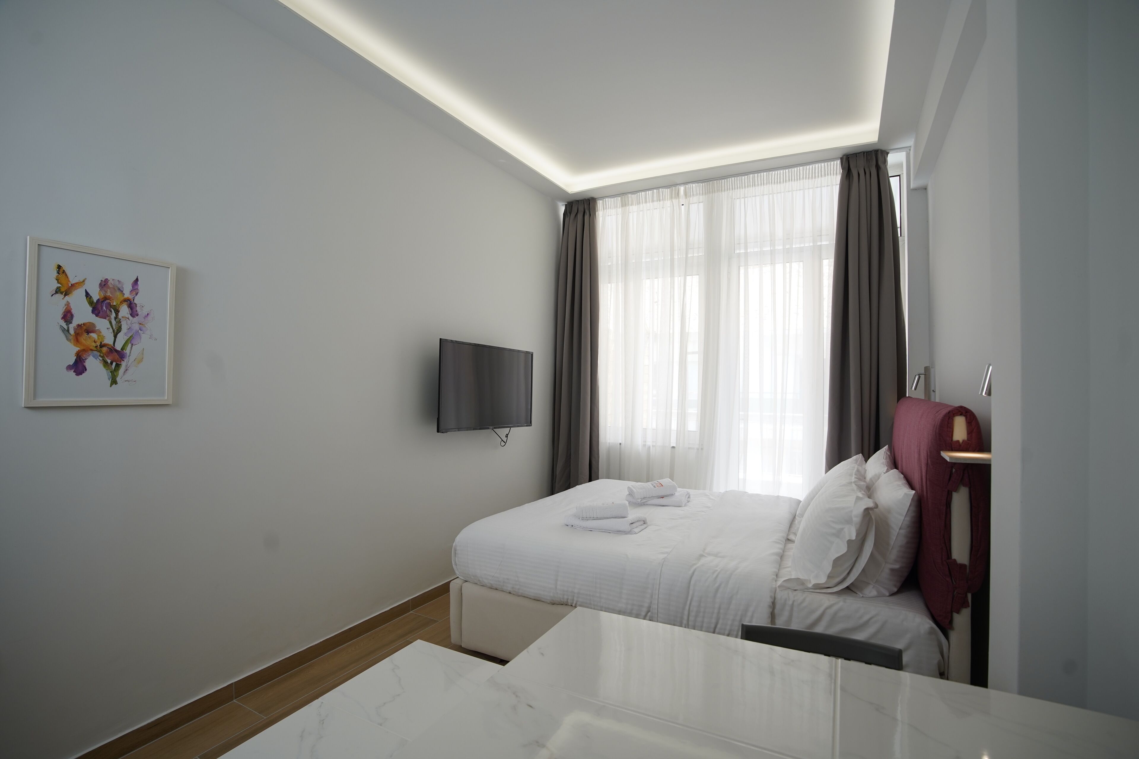 A hotel room with a bed, a flat-screen TV, a painting, and a window with curtains.
