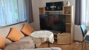 Uma sala de estar com sofá, mesa de centro, TV e alto-falantes.