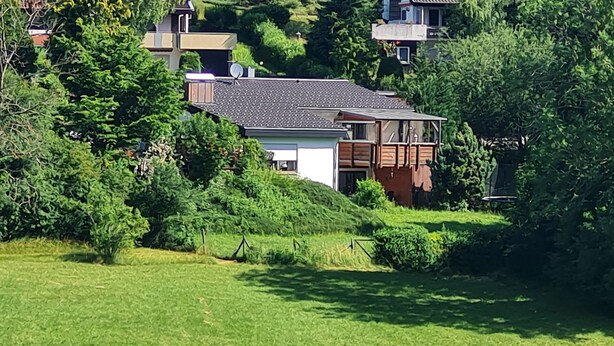 Um bairro residencial com uma casa rodeada por vegetação exuberante e outras casas ao fundo.