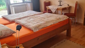 Quarto com cama de madeira, escrivaninha com cadeira, radiador e janela.