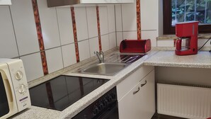 Cozinha com armários brancos, fogão preto, micro-ondas, pia e cafeteira vermelha.