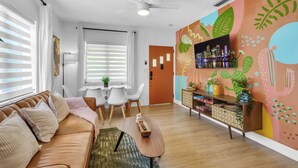 A modern living room with a brown leather sofa, a wooden coffee table, and a colorful mural on the wall.
