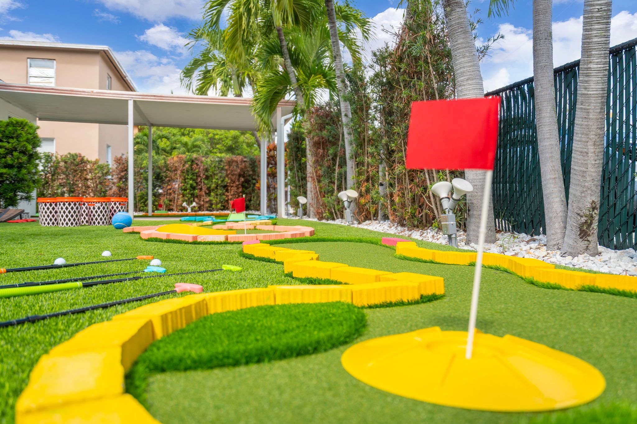 A miniature golf course with a red flag, green grass, and palm trees.