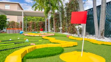 A miniature golf course with a red flag, green grass, and palm trees.