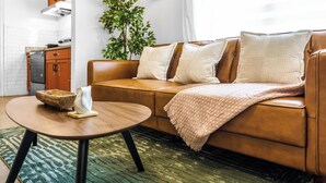 Ein Wohnzimmer mit einem braunen Ledersofa, einem runden Holztisch und einem Teppich mit grünem Muster.