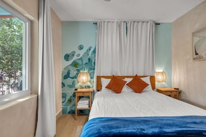 A bedroom with a bed, two bedside lamps, a nightstand, a window with curtains, and a wall with a leaf pattern.