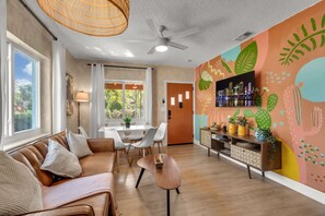 A modern living room with a sofa, dining table, and chairs, a ceiling fan, and a vibrant wall mural.