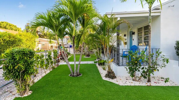 A well-maintained garden with palm trees and artificial grass in front of a white building with a balcony.