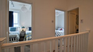 A hotel room with two beds, a small table, and a chair. There is a window with curtains and a ceiling light fixture. - Ard na Mara- Coastal Apartment (Pittenweem)