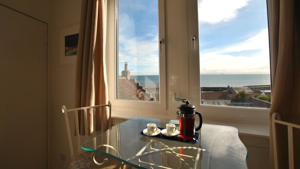 A room with a glass table, two chairs, a coffee maker, and a view of the sea through a window. - Ard na Mara- Coastal Apartment (Pittenweem)