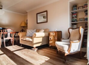 A living room with a sofa, armchairs, a wooden coffee table, a lamp, and a bookshelf.