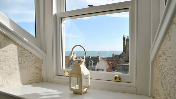 A window with a view of the sea and buildings, a white lantern on the sill, and a map on the wall.