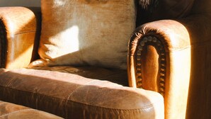 A brown leather armchair with a plaid throw blanket and a cushion.
