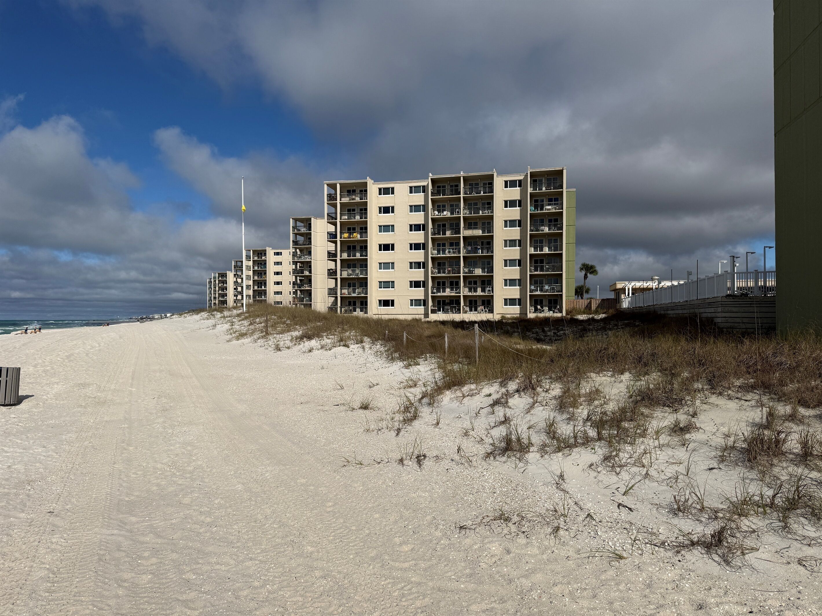 Een strandhotel met meerdere verdiepingen, een zandstrand op de voorgrond en een bewolkte lucht.