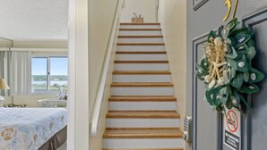A staircase leading to a room with a bed, a window, and a door with a decorative wreath.