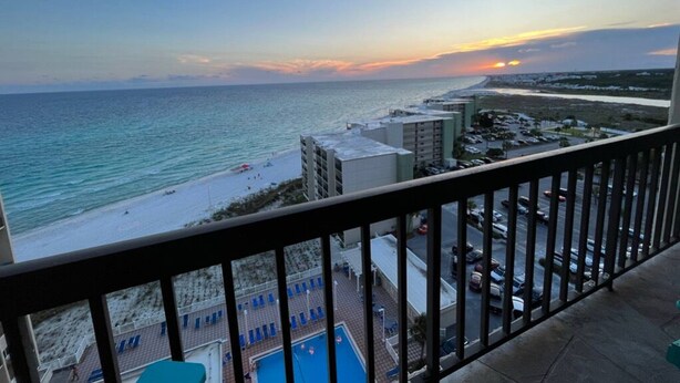 A balcony with a view of a beach and ocean during sunset.