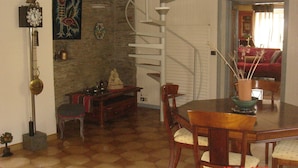 Un comedor con una mesa de madera, sillas, una escalera de caracol, un reloj y un cuadro en la pared.