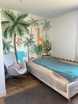 Quarto com cama, cadeira de balanço, tapete cinza e um mural na parede com girafa, macaco e elefante.