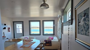 A modern kitchen with a wooden island, bar stools, and a view of the sea through large windows. - Oceanfront Apartment, Gros Morne View in the heart of Park (Rocky Harbour)