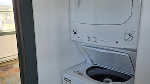 A compact, white front-loading washer and dryer unit with a control panel featuring multiple settings and a label indicating energy efficiency. - Oceanfront Apartment, Gros Morne View in the heart of Park (Rocky Harbour)