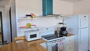 A modern kitchen with white appliances, a wooden table, and a teal hood. - Oceanfront Apartment, Gros Morne View in the heart of Park (Rocky Harbour)
