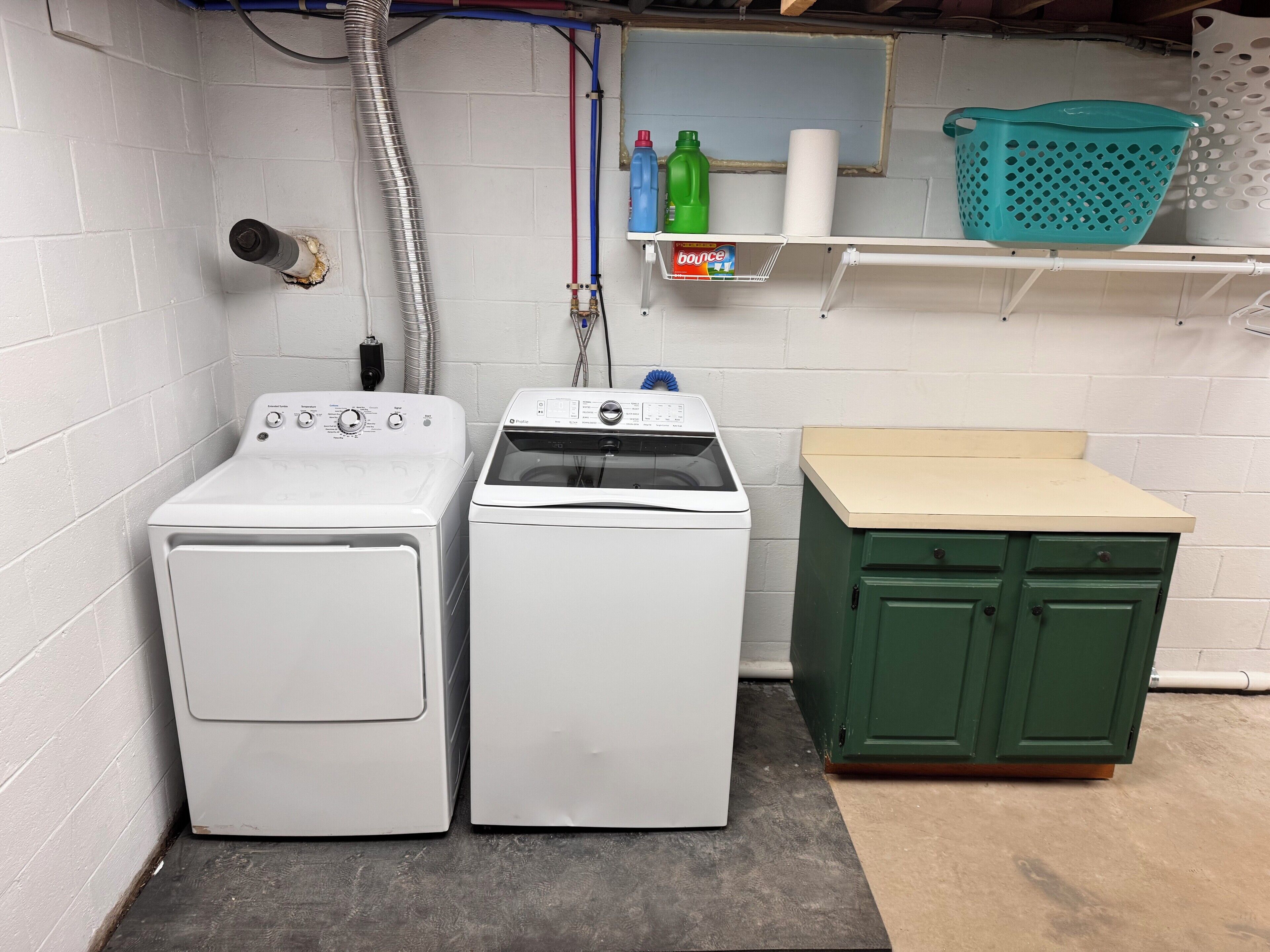 A laundry room with two white front-loading washers, a green cabinet, and a shelf with laundry supplies.