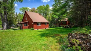 Une cabane en bois rouge, dotée d’un toit en pente, entourée d’une pelouse verdoyante et luxuriante et d’arbres.