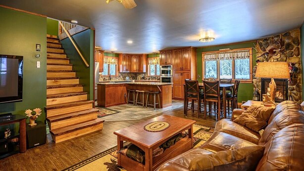 Un salon spacieux avec un canapé en cuir, une table basse en bois et un escalier menant à une cuisine équipée de meubles en bois et dotée d’une cheminée en pierre.