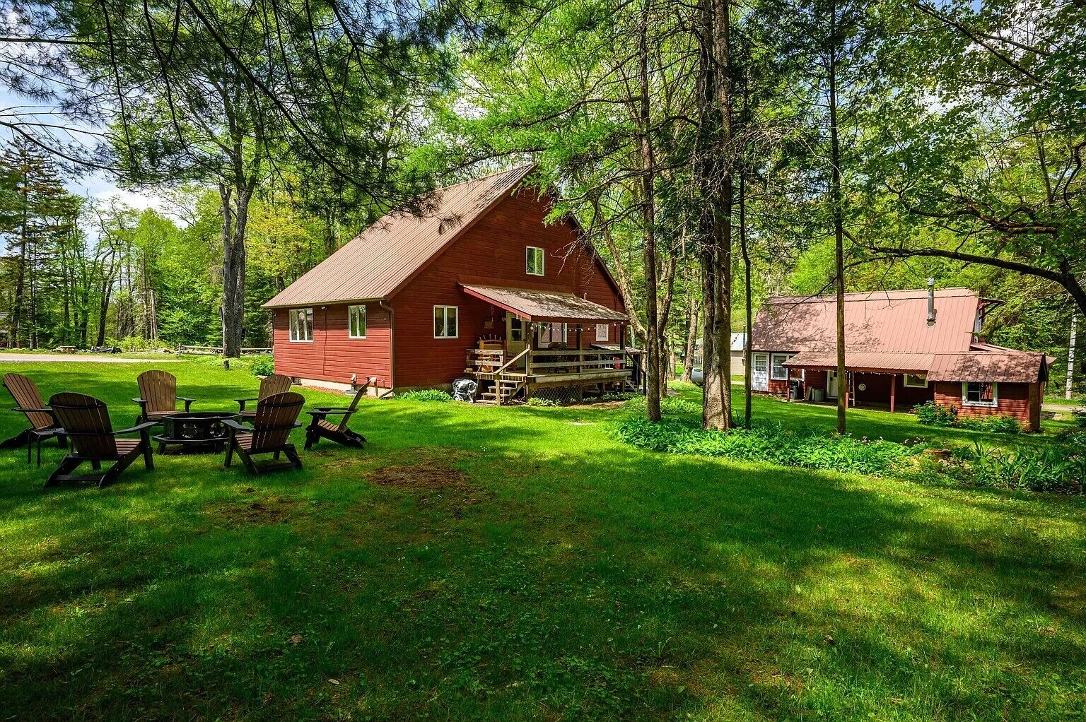 A rustic cabin with a porch, surrounded by a lush green lawn and trees.