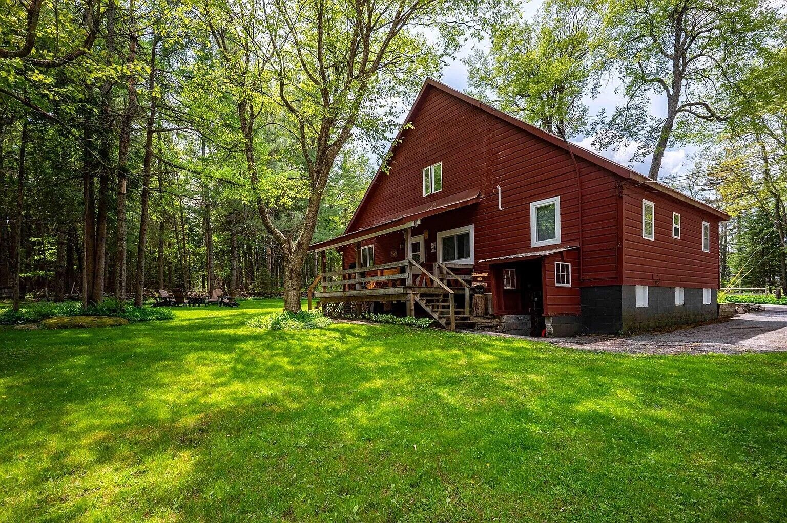 A red wooden cabin with a porch, surrounded by a forest.