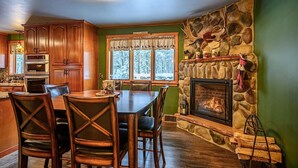 Une cuisine chaleureuse avec des meubles en bois, une cheminée en pierre et un coin repas comprenant une table et des chaises.