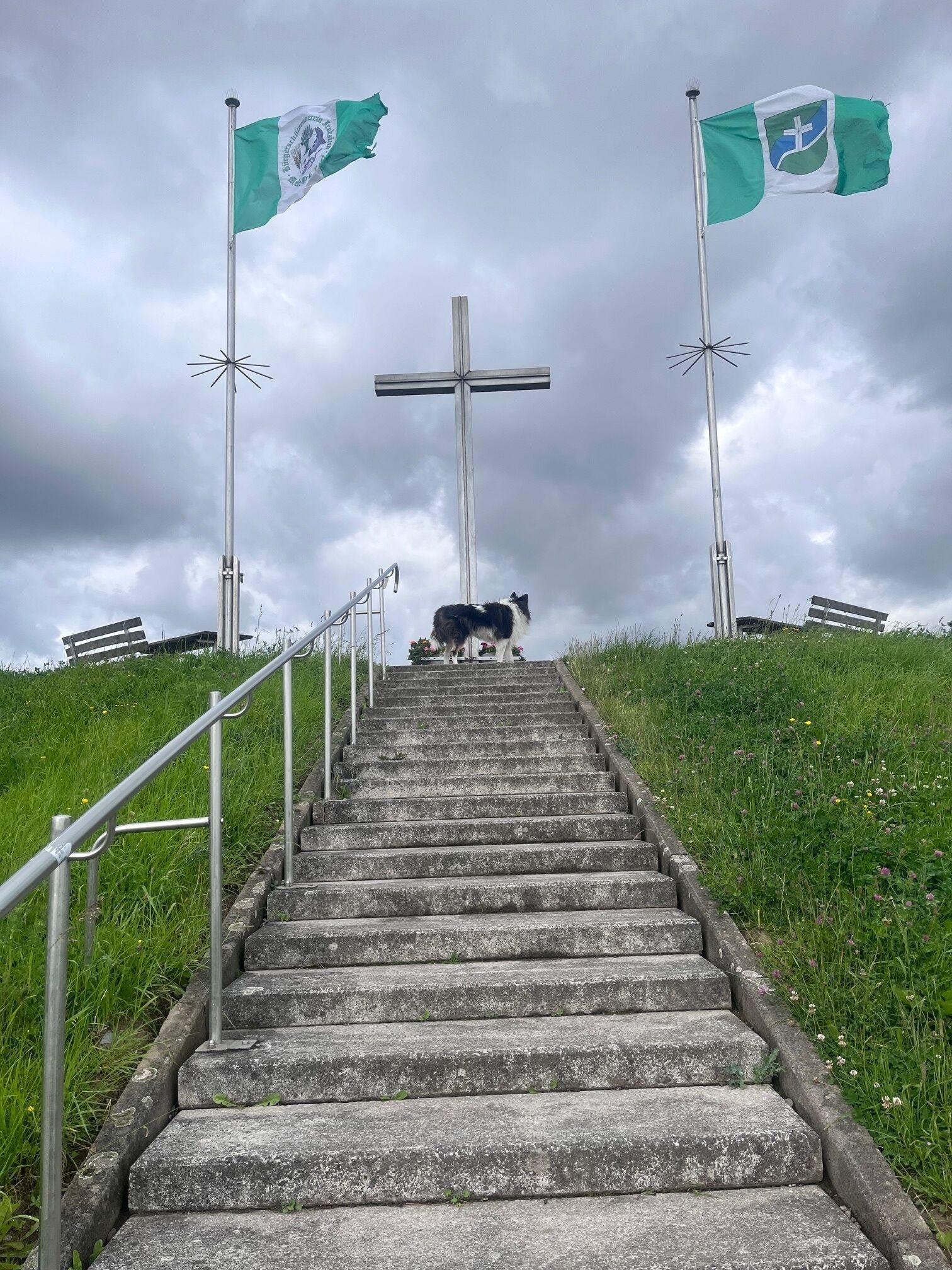 A set of concrete stairs leading up to a large cross, with two flags on either side.