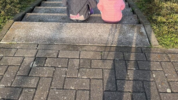 Two children sitting on a paved path with a view of a body of water and greenery in the background. - --Niederrhein Kaue-- your cozy vacation apartment directly behind the dike. (Voerde (Niederrhein))