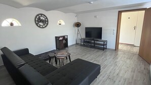 A modern living room with a large black sectional sofa, a small table, and a TV. - --Niederrhein Kaue-- your cozy vacation apartment directly behind the dike. (Voerde (Niederrhein))