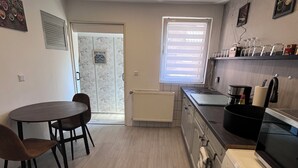 A compact kitchen with a dining area, featuring a built-in oven, a coffee machine, and a window with blinds. - --Niederrhein Kaue-- your cozy vacation apartment directly behind the dike. (Voerde (Niederrhein))