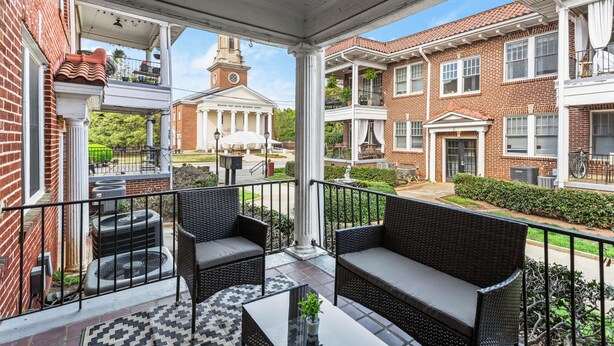 A covered balcony with wicker furniture and a view of a historic building. - Charming 2-bedroom apartment in dowtown Decatur/ 20 min from downtown ATL (Decatur)