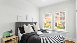 A bedroom with a bed, a nightstand, a window with blinds, and a view of buildings outside. - Charming 2-bedroom apartment in dowtown Decatur/ 20 min from downtown ATL (Decatur)