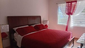 Une chambre avec un grand lit, une table de chevet, une table et une fenêtre avec des rideaux.
