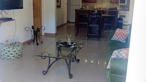 Un salon avec une table basse en verre, un canapé, un téléviseur et un ventilateur de plafond.