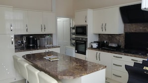 A modern kitchen with white cabinets, a marble countertop, a built-in oven, and a microwave.