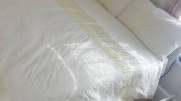 Cama com roupa de cama branca e cabeceira de madeira.