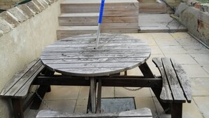 A wooden picnic table with benches, a brick wall, and a door leading to a building.